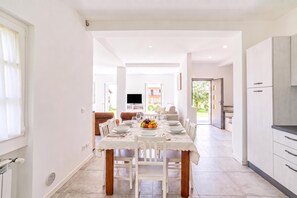 A modern dining area with a table set for four, a kitchen with cabinets, and a living area with a sofa and TV.