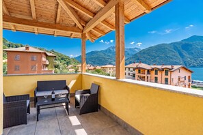 A balcony with wicker furniture and a table, overlooking a mountainous landscape and a body of water. - Casa Veligato 2 (San Siro)