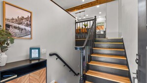 Una escalera moderna con escalones de madera y barandal negro, que conduce a una zona de cocina con encimera de madera y un cartel de bienvenida enmarcado.
