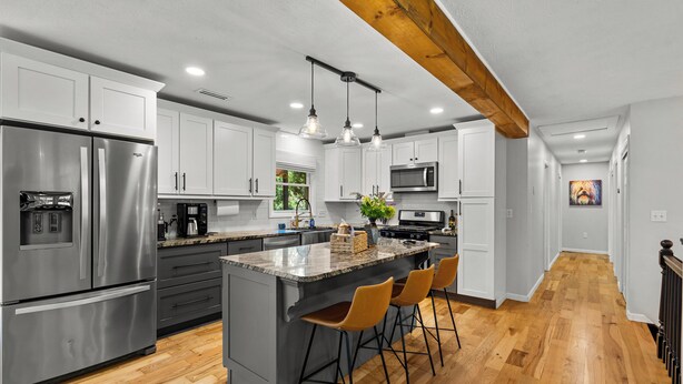 Una cocina moderna con electrodomésticos de acero inoxidable, una isla central con taburetes de bar y una viga de techo de madera.
