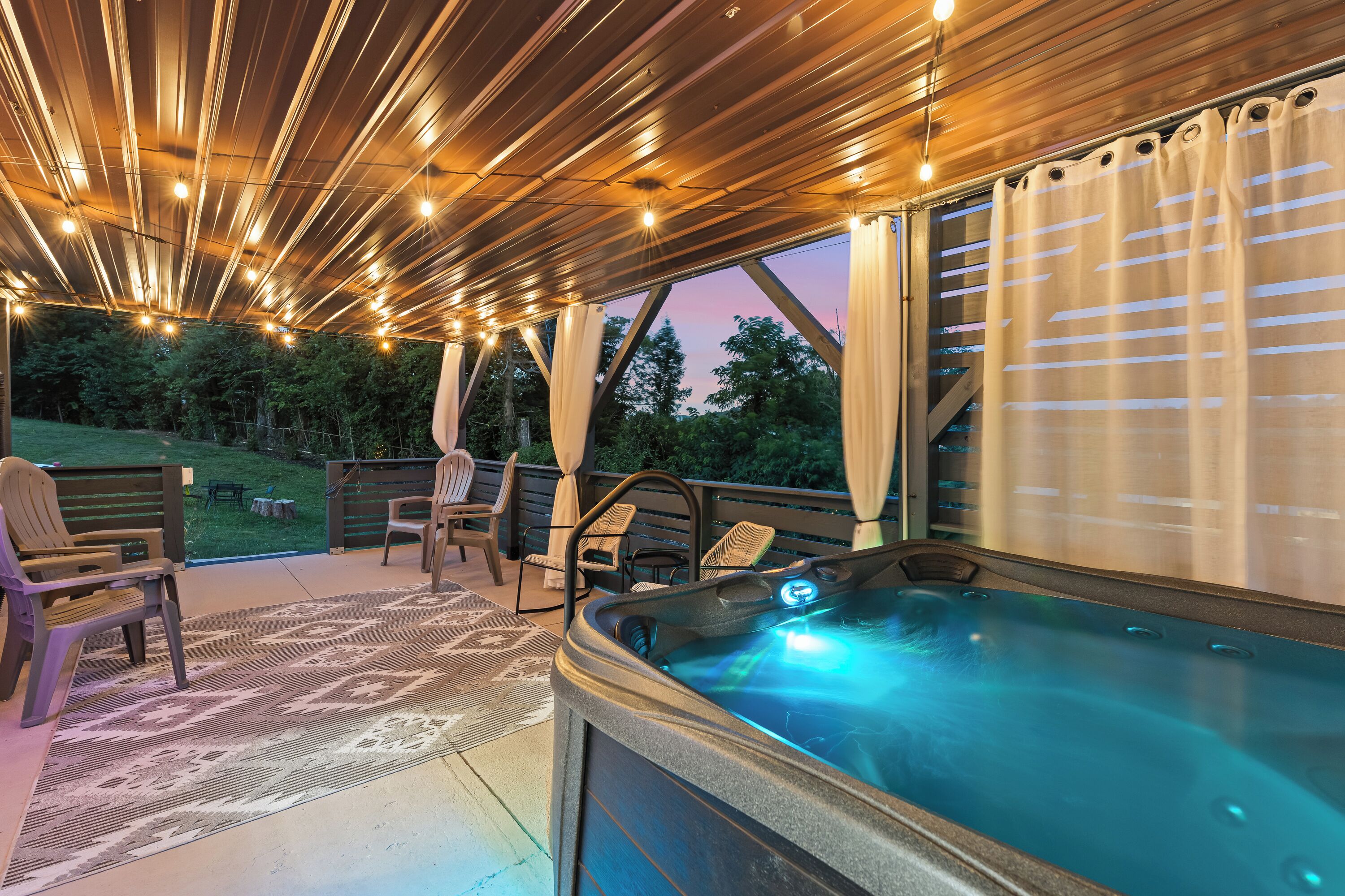 An outdoor hot tub area with a wooden deck, chairs, and string lights.