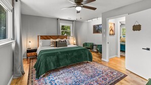 Un dormitorio con cama, ventilador de techo, ventana y puerta que da a otra habitación.