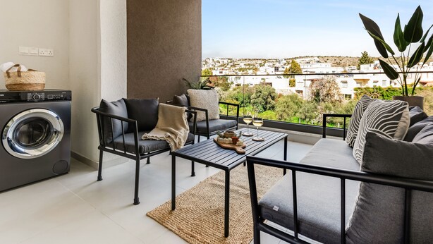 A balcony with a washing machine, seating area, and a view of the city. - Sanders Triple - Cozy 1-bdr Apt With Balcony (Limassol)