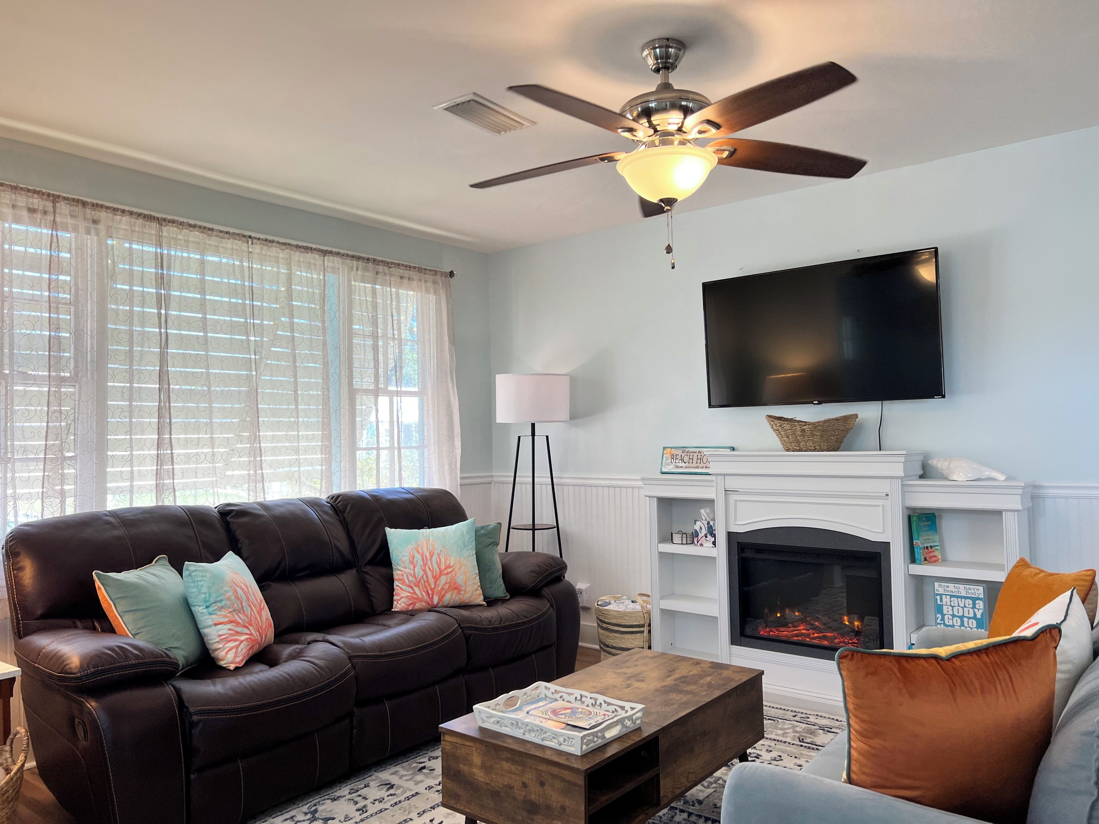 A living room with a leather sofa, a wooden coffee table, a fireplace, and a ceiling fan.