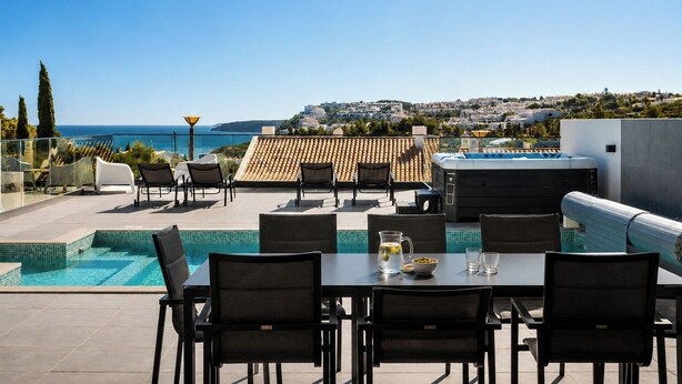 Un área de piscina en la azotea con mesa y sillas, un jacuzzi y vistas al mar y al pueblo.