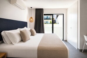 Quarto de hotel com cama, luminária pendente, vista por uma porta e uma cadeira branca.