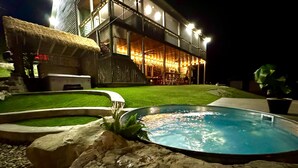 A swimming pool with a hot tub, a thatched-roof structure, and a building with illuminated windows at night. - “Triple Timbers” 18 bdrm,sleeps 56! hotubs, docks, 5 firepits, sxs, rent boats (Lafollette)