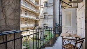 Un balcón con una mesa y sillas de madera, que da a un patio con edificios.