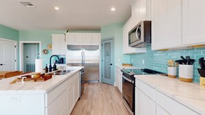 A modern kitchen with white cabinets, a stainless steel refrigerator, a microwave, and a tiled backsplash. - Tiffany House: 4  BR, 3.5  BA House in Crystal Beach, Sleeps 16 (Bolivar Peninsula)