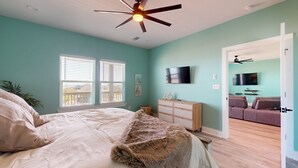 A bedroom with a bed, a ceiling fan, a TV, and a view of the living room. - Tiffany House: 4  BR, 3.5  BA House in Crystal Beach, Sleeps 16 (Bolivar Peninsula)