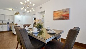 A modern dining area with a glass table set for four, surrounded by dark upholstered chairs. A contemporary chandelier hangs above, and a painting adorns the wall. - Floridays Resort Retreat | Relax & Explore Orlando (orlando)