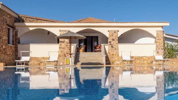 A poolside area with a clear view of a building with stone pillars and a tiled roof. - Chic Villa Antonina One Bedroom No2176 (Golfo Aranci)