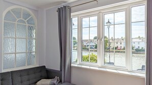 A room with a grey sofa, a large window with a view of a river and buildings, and a decorative ceiling light. - Grace Cottage - Emsworth -  a cottage that sleeps 6 guests  in 3 bedrooms (Emsworth)