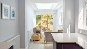 A modern kitchen with a skylight, a dining area with a table and chairs, and a view of the garden through glass doors. - Grace Cottage - Emsworth -  a cottage that sleeps 6 guests  in 3 bedrooms (Emsworth)