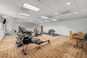 Ein Fitnessraum mit unterschiedlichen Trainingsgeräten, einem großen Fenster und einem Konferenztisch mit Stühlen.