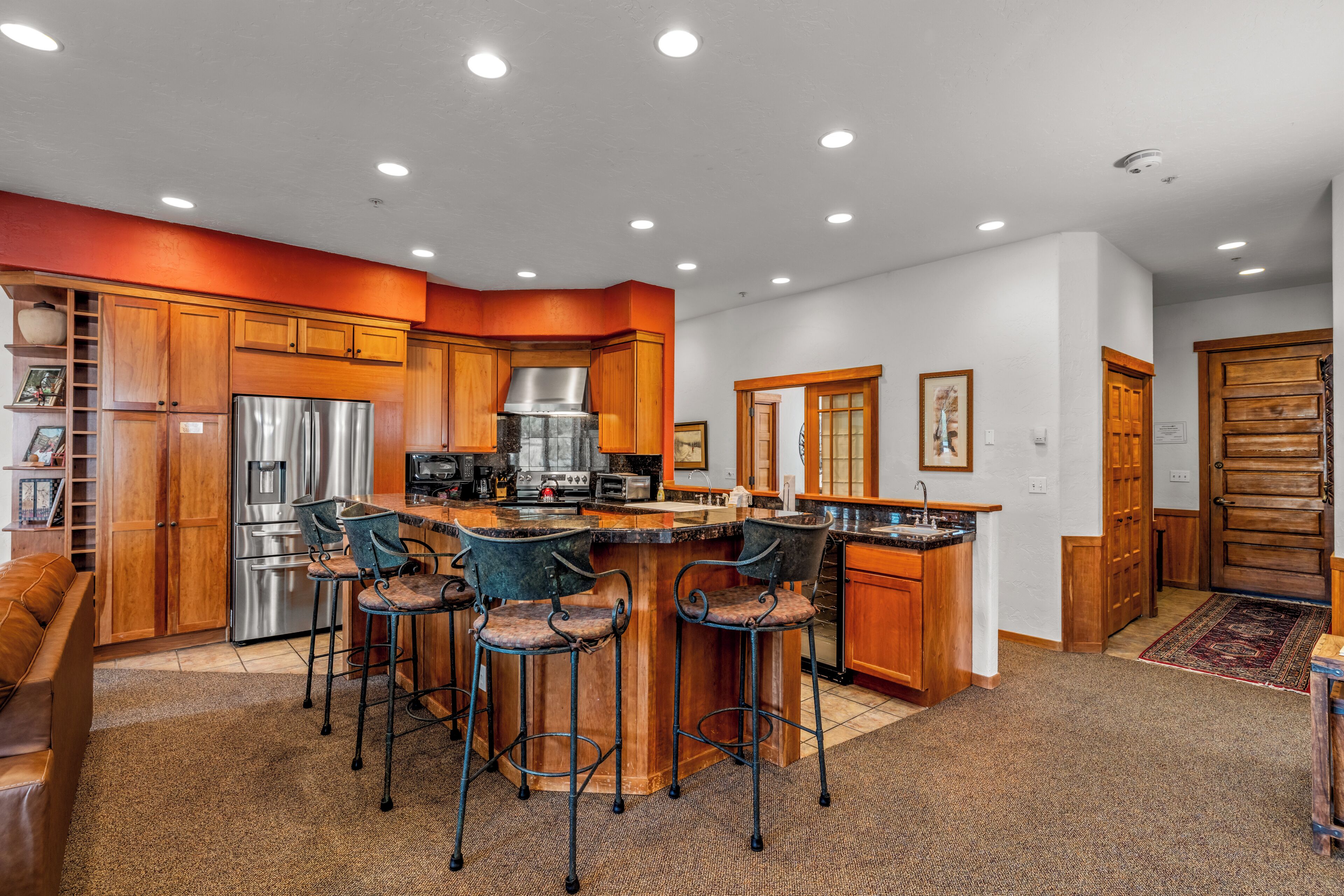 A modern kitchen with a central island, bar stools, stainless steel appliances, and wooden cabinetry.