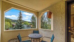 Un balcón con una mesa y sillas, vista a casas y árboles, y una pared con textura.