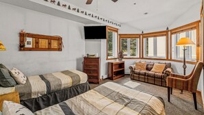 Una habitación acogedora con una cama, un sofá, una silla, un armario de madera y un televisor.