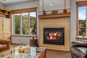 A living room with a fireplace, a large window with a view of the outdoors, and a leather sofa. - Luxury Mountain Escape| The Terraces at EagleRidge! (Steamboat Springs)