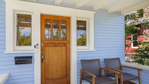 Una casa blu con una porta d'ingresso in legno, due finestre e una panchina all'esterno.
