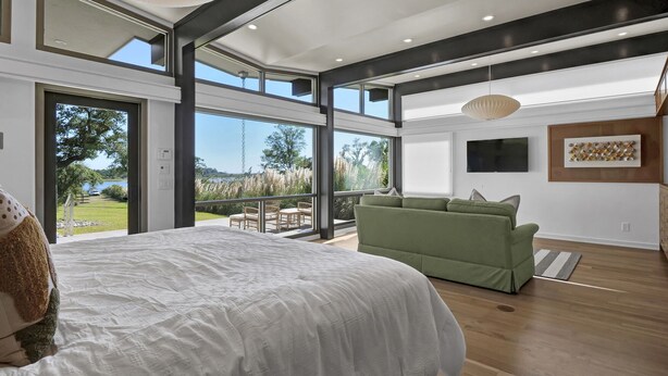 A modern bedroom with a large bed, a green sofa, and a balcony with a view of the outdoors. - Waterfront Oasis: Dock, Recreation Hall & Pet-Friendly! (Wilmington)