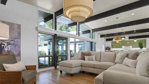 A spacious living room with a large sectional sofa, a wicker chair, and a dining area with pendant lights. - Waterfront Oasis: Dock, Recreation Hall & Pet-Friendly! (Wilmington)
