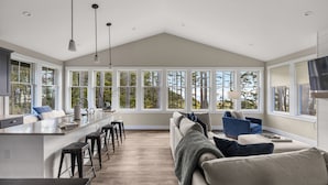 A spacious kitchen with a large island, bar stools, and a view of the outdoors through large windows. - Seabrook Seaclusion | Pet Friendly, Ocean View 4BR | Sleeps 10, Elevator (Pacific Beach)