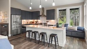 A modern kitchen with a central island, bar stools, and a built-in bench with cushions. - Seabrook Seaclusion | Pet Friendly, Ocean View 4BR | Sleeps 10, Elevator (Pacific Beach)