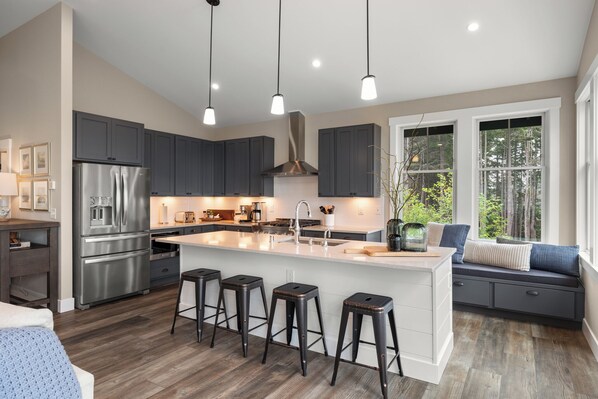 A modern kitchen with a central island, bar stools, and a built-in bench with cushions. - Seabrook Seaclusion | Pet Friendly, Ocean View 4BR | Sleeps 10, Elevator (Pacific Beach)