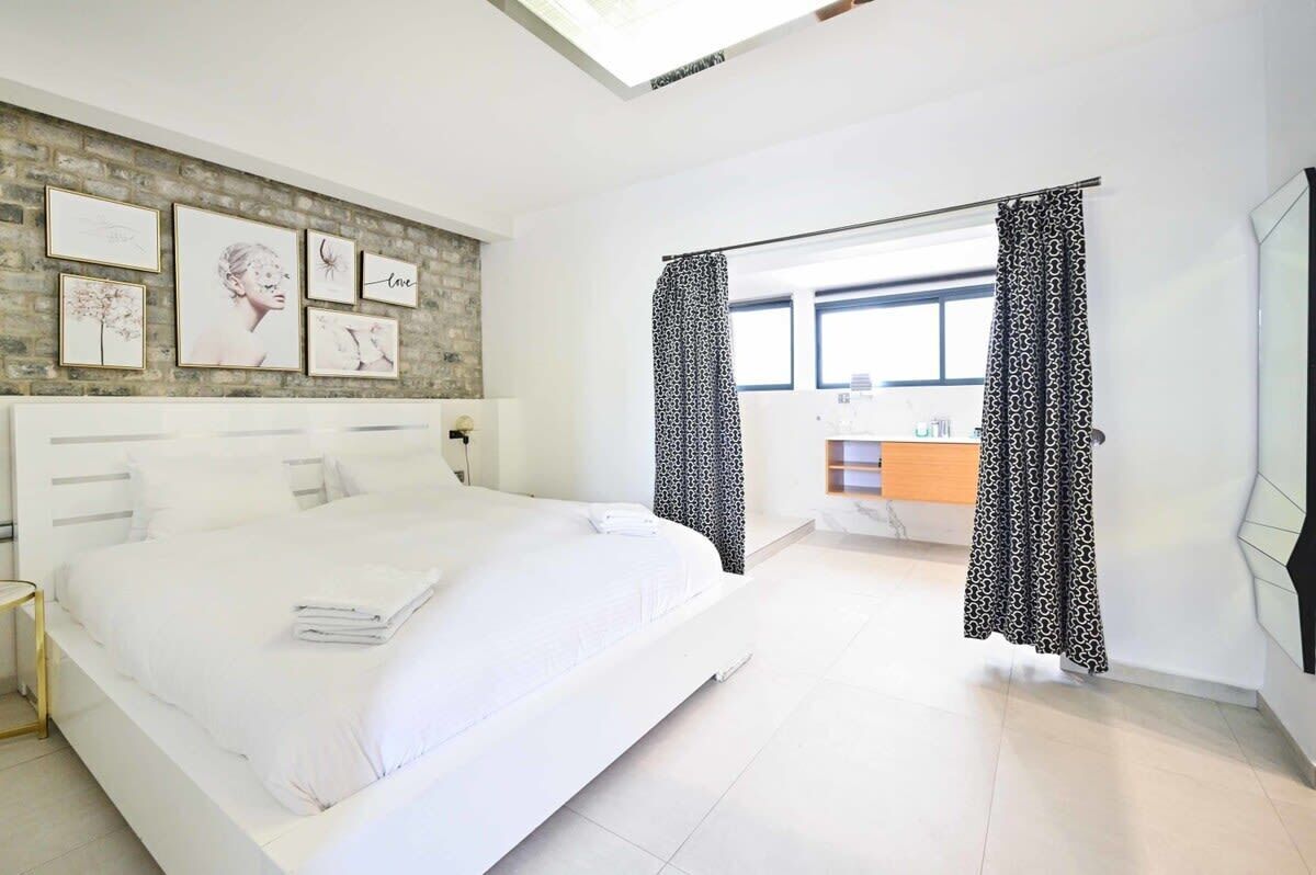 A modern hotel room with a large bed, a brick accent wall, and a view of the bathroom.