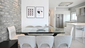 Un espace repas moderne avec une table en verre, des chaises à revêtement gris et un mur en briques.