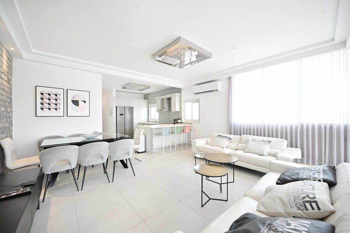 A modern living room with a dining area, a sofa set, and a kitchen in the background.