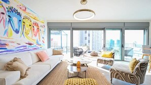 Un salon moderne doté d’une grande fenêtre, d’un canapé blanc, d’un fauteuil à rayures et d’un tableau abstrait aux couleurs vives accroché au mur.