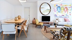 Un salon moderne comprenant un coin repas, un ensemble de canapés, un téléviseur et un tableau abstrait aux couleurs vives.