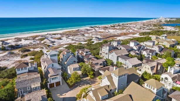 Uma área residencial costeira com casas, uma praia e um céu azul claro.