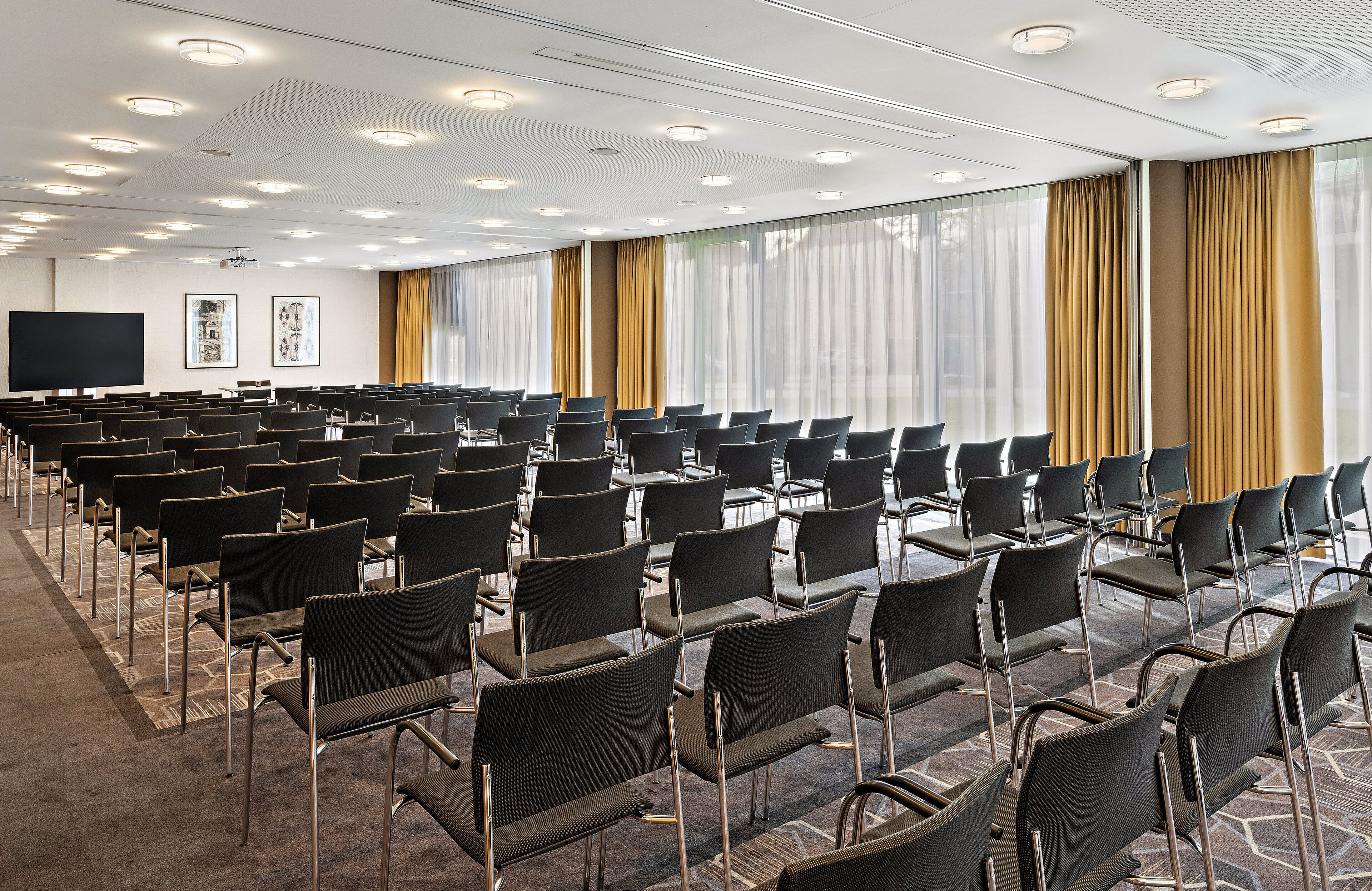 A conference room with rows of chairs, a projector screen, and large windows with curtains.