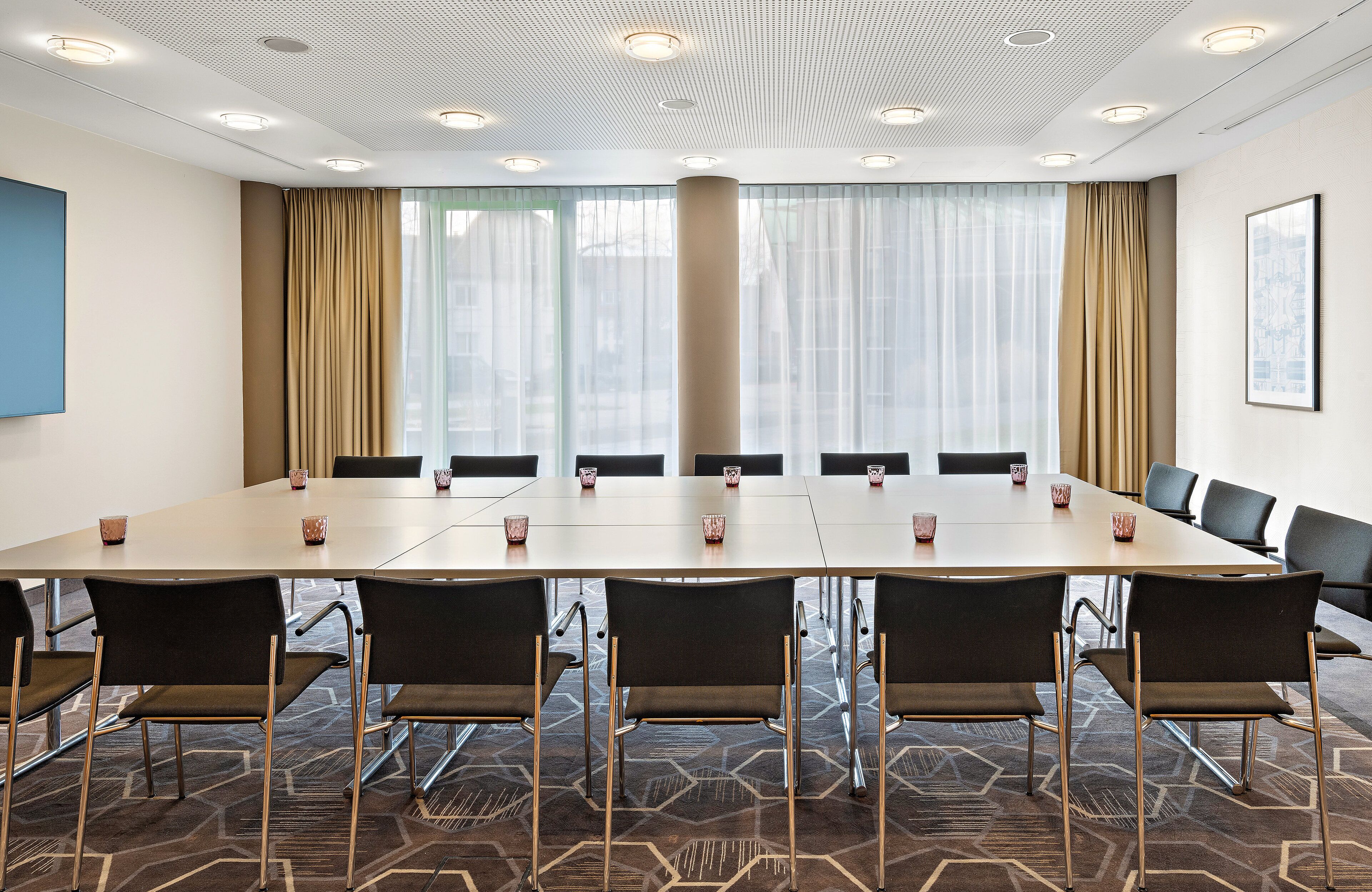 A conference room with a long table, chairs, and a large window with curtains.