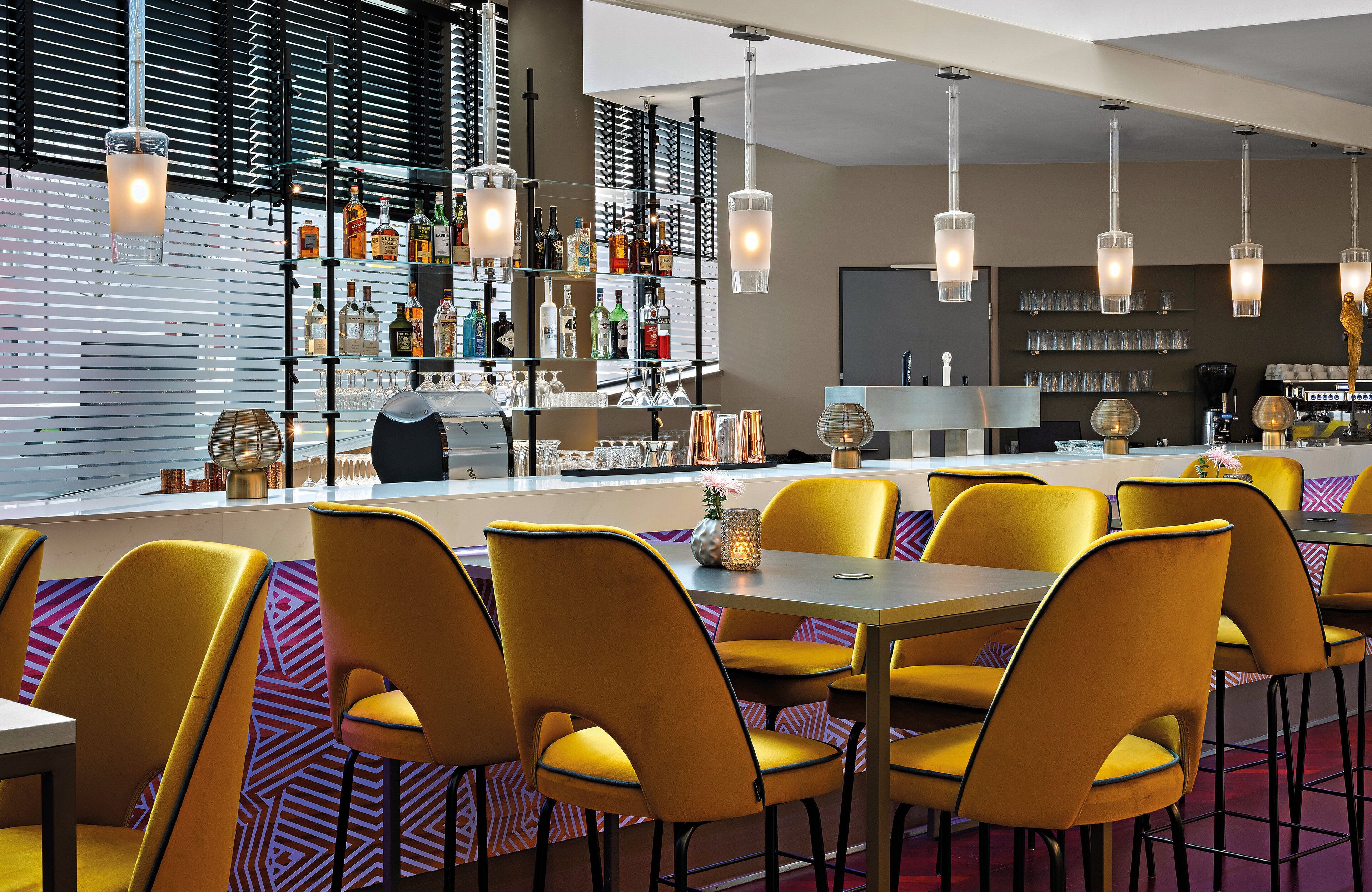 A modern bar area with yellow chairs, a bar counter, and various bottles and glasses.