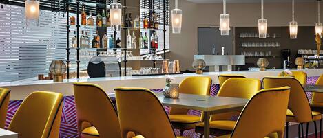 A modern bar area with yellow chairs, a bar counter, and various bottles and glasses.