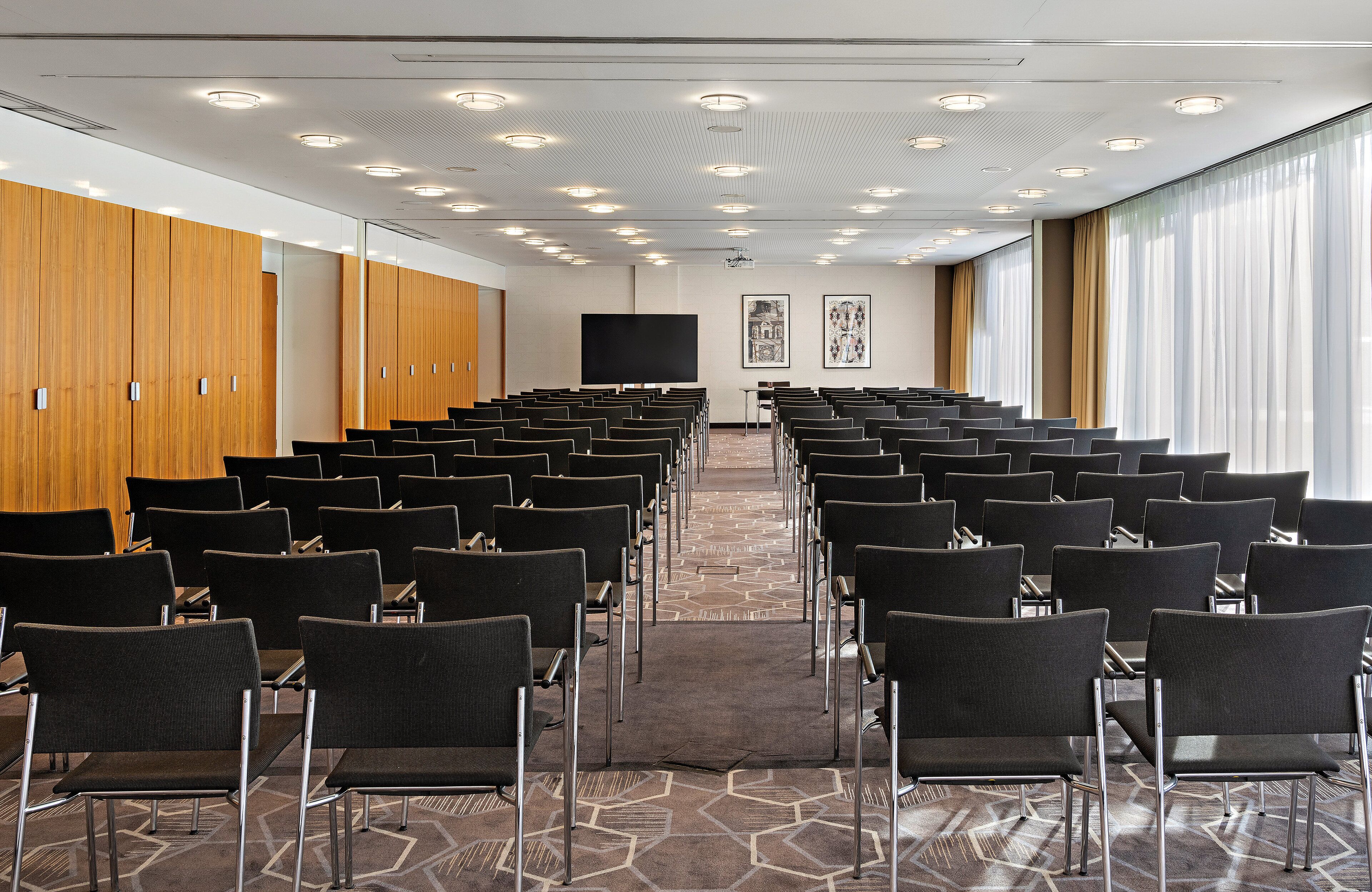 A conference room with rows of chairs, a large screen, and wooden lockers.