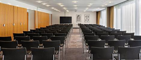 A conference room with rows of chairs, a large screen, and wooden lockers.
