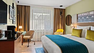 Habitación de hotel con una cama grande, un escritorio con silla, televisor y ventana con cortinas.