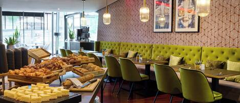 A restaurant with a green upholstered booth, multiple dining tables, and chairs. There are various food items displayed on the tables.