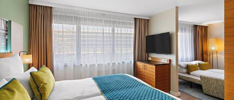 A hotel room with a large bed, a smaller bed, a TV, a desk, and a window with curtains.