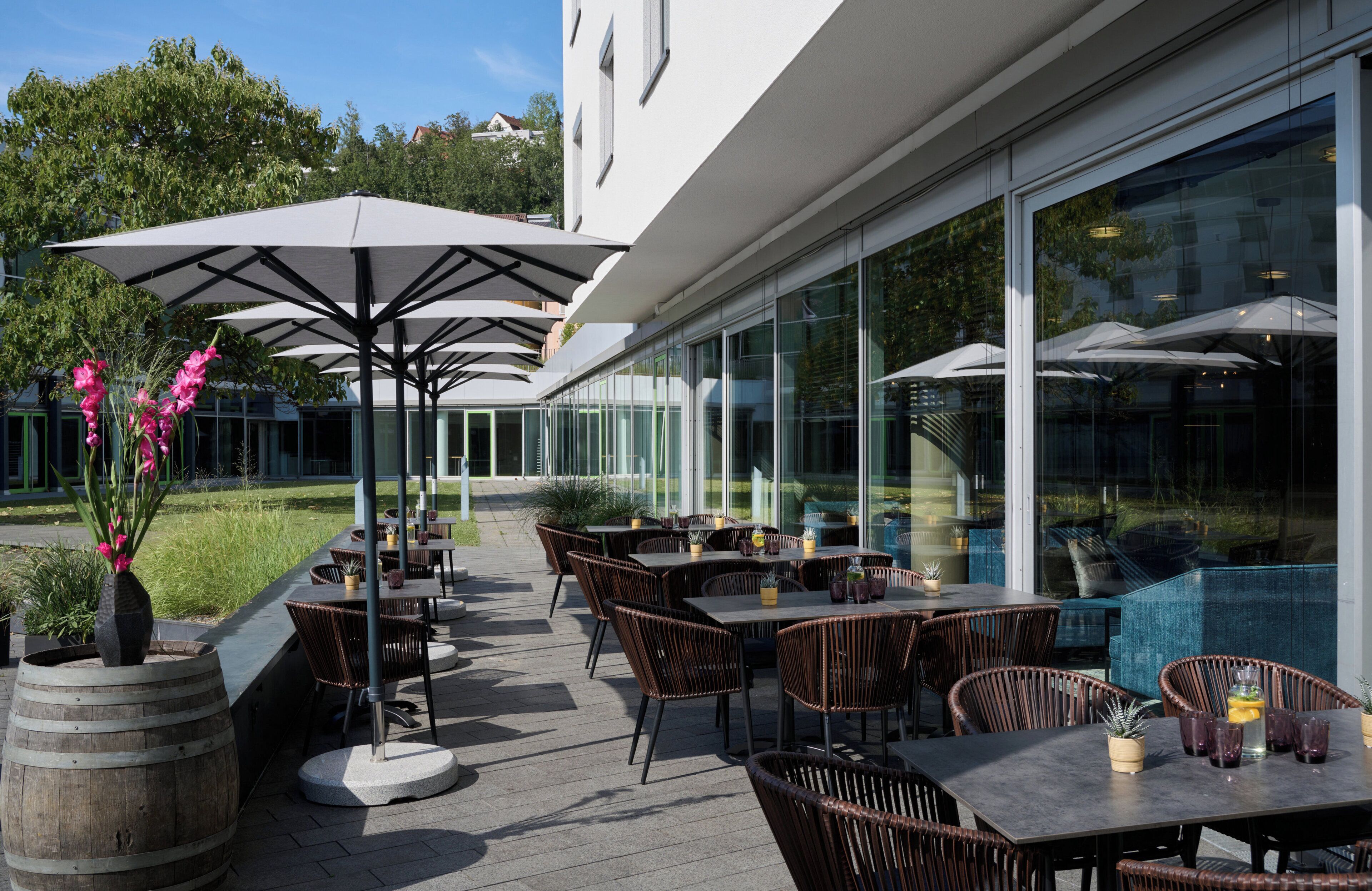 An outdoor patio with tables and chairs, umbrellas, and potted plants.