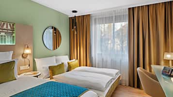 A hotel room with two beds, a desk, a chair, a round mirror, and a window with curtains.
