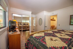 A bedroom with a large bed, a television on a wooden stand, a chair, and a door leading to another room.