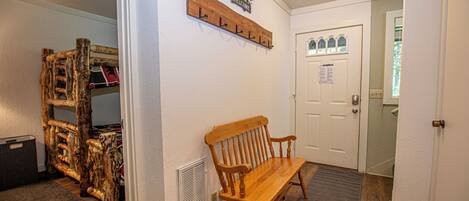 A hallway with a wooden bench, a coat rack, and a door with a window.