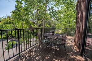 A wooden deck with a round table and chairs, surrounded by a metal railing.