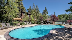 A swimming pool with lounge chairs and umbrellas, surrounded by trees and a building. - St. Francis # 18 by Hauserman Rentals (Tahoe City)
